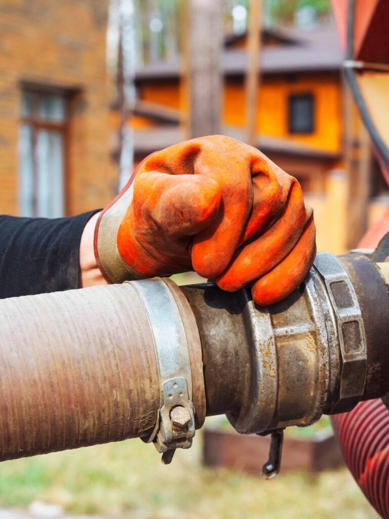 a hand connects a suction hose to a sewage tanker truck. Sewer pumping machine. Septic truck. Pumping wastewater from a septic tank. Septic tank maintenance