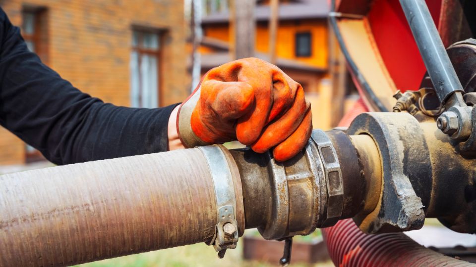 a hand connects a suction hose to a sewage tanker truck. Sewer pumping machine. Septic truck. Pumping wastewater from a septic tank. Septic tank maintenance